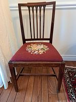 Front view of a single chair showing carved back, rope-twist top rail, and floral needlepoint seat cover