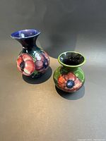 Both Moorcroft vases shown side by side front view on dark background