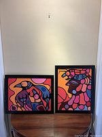 Both framed paintings side by side on table against wall