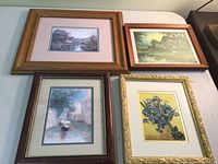 Four framed prints displayed on a surface: two English thatched cottages by riverside, one gondola on water scene, and one iris flowers in a vase still-life print