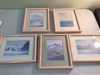 Five Scotland-themed watercolor prints in pale pink frames on table, arranged with four flat and one propped 