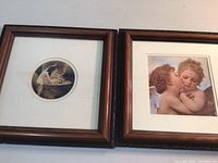Photo showing both framed prints side by side, showing cherub artwork and wood frames