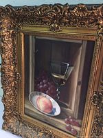 Frontal view of the framed still life painting emphasizing the intricate carved gold frame and visible painting details.