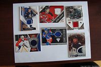 Front side view of 6 NHL jersey trading cards arranged on white paper showing colored jersey swatches.