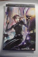 Front cover of Black Widow #1 comic with Stan Lee tribute and Clayton Crain cover art showing Black Widow in black tactical outfit with guns in a cityscape.