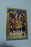 Front view of a gold-bordered Chris Bosh rookie basketball card showing him on court in Toronto Raptors uniform, dribbling a basketball with gold and blue accents.