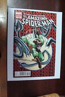 Front cover of The Amazing Spider-Man #700 Variant Edition comic showing Doctor Octopus and a man in a green shirt on his mechanical arms, red background with repeated 700.