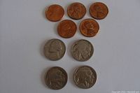 Six pennies from different years and four Buffalo nickels arranged on a flat surface, showing both coin types in used condition.