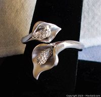 Front view of the adjustable sterling silver ring shaped like two calla lily flowers with clear stone centers on black display stand.