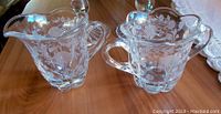 Front angle of both etched leaded crystal sugar bowl and creamer on wooden table.