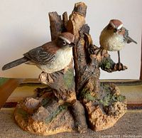 Close-up view of two bird sculptures perched on detailed, textured tree stump bases used as bookends.