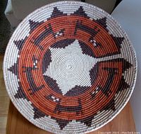 Top view of circular Native American pictorial basket showing detailed woven star and geometric patterns in natural, rust, and brown colors.