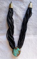 Full view of the multi-strand necklace showing black bamboo beads and bronze end caps, with the turquoise centerpiece visible at the bottom of the strands.