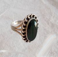 Top angle showing the polished oval black onyx stone set in a decorative scalloped bezel on sterling silver ring.
