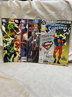 Photo featuring seven DC Comics comic books displayed upright in a row on a light surface with a beige curtain background.