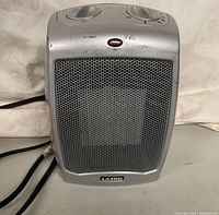 Front view of silver Lasko portable heater showing mesh grille, top control knobs, and branding.