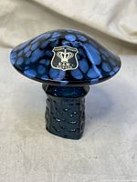 Side view of blue spotted hand blown glass mushroom with Golden Crown E&R Sweden label attached to cap.