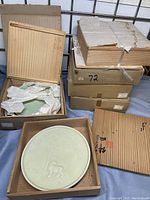 Six wooden presentation boxes stacked with one box open displaying a light green celadon plate wrapped in tissue paper.