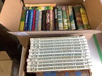 Top view of a box containing an arranged set of hardcover books with colorful spines, mainly novels and miscellaneous titles.