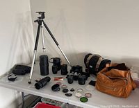 Wide view of lot showing Pentax cameras, lenses, multiple lens filters, two camera bags, and Sony tripod arranged on table.