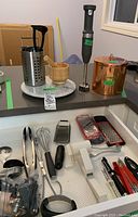 Overview of copper canister, marble Lazy Susan, wooden mortar and pestle, immersion blender, and some kitchen utensils in drawer.
