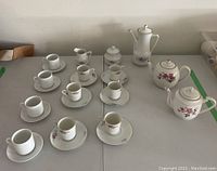 Full view of the tea and coffee set arranged on table with cups, saucers, coffee pot, teapots, creamer, sugar bowl.