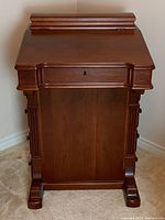 Front view of closed desk showing keyhole on hinged writing surface and fluted column supports
