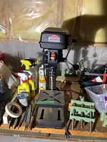 Full front view of Jobmate drill press with metal base plate, visible power cord, handle, and surrounding workshop items.