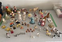 Wide view of various porcelain and ceramic figurines, animal figures, and salt and pepper shakers spread on white table
