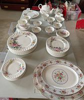 Overview of mixed Royal Albert swirl-edge floral plates, bowls, cups, saucers, and Royal Doulton Arcadia platters