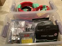 Photo of one tote showing bundles of red and black speaker wires and various small packaged components including connectors.