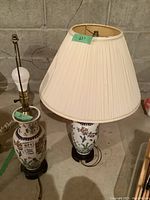 Two matching ceramic table lamps, one with pleated cream shade, both with floral and bird designs on ceramic bases with wooden stands.