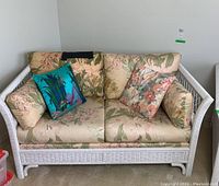 Front view of the white painted Henry Link wicker loveseat with floral patterned cushions and colorful throw pillows.