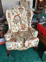 Front view of the upholstered wingback chair showing floral crewel embroidery and cabriole legs