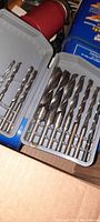 Set of multiple steel drill bits in gray plastic case, various sizes, arranged neatly inside box