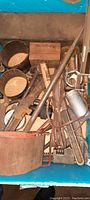 Box containing various antique tools including monkey wrenches, metal rods, small hand tools, and wooden handled wrenches.