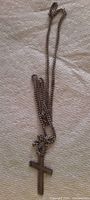 Photo of the whole necklace laid flat on a light textured fabric background showing the chain and cross pendant in full view.