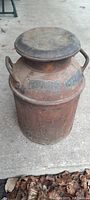 Full view of an old metal milk can with lid showing rust and two handles.