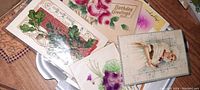 Photo shows multiple antique embossed postcards with floral and greeting themes, including roses and birthday greetings.