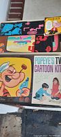 Box top showing Popeye cartoon character and image of children playing with the kit, with colorful cartoon pieces arranged inside the box