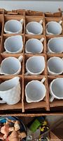 Twelve white milkglass creamer cups arranged in original cardboard box with individual dividers