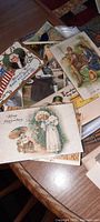 Top view showing multiple vintage postcards with embossed designs including a political themed card with a US flag, a Victorian woman with flowers, and a military scene.