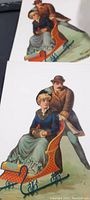 Two Victorian cardstock die cuts showing a man and woman on a sled, measuring approx. 10 inches tall, bold colors, as found condition.