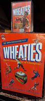 Photo showing the large Wheaties Sports Trivia Game box and the small Muhammad Ali Wheaties mini cereal box in a clear case on top of it.