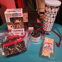 Multiple items displayed on table including Funko Pop, popcorn phone case, Cisco charger, headphones, and tumbler