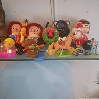 Wide shot of all toys on a shelf, showing Raggedy Ann dolls, rubber duckies, Care Bear piggy bank, horses and other figures