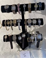 Photo showing large lot of 21 assorted wristwatches displayed on black stand, varying band types, colors, and dial shapes.