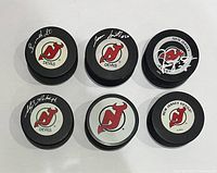 Top view of six hockey pucks, four with New Jersey Devils logos and player signatures, two commemorative pucks with special designs and autographs.