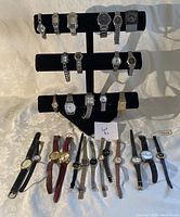 Full view showing three rows of watches on black display stand and watches laid flat in front on fabric surface