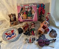 Overview photo showing all clown paraphernalia including jack in the box, puppet heads, mini violin, clown figurines, commemorative plate and paper insert
